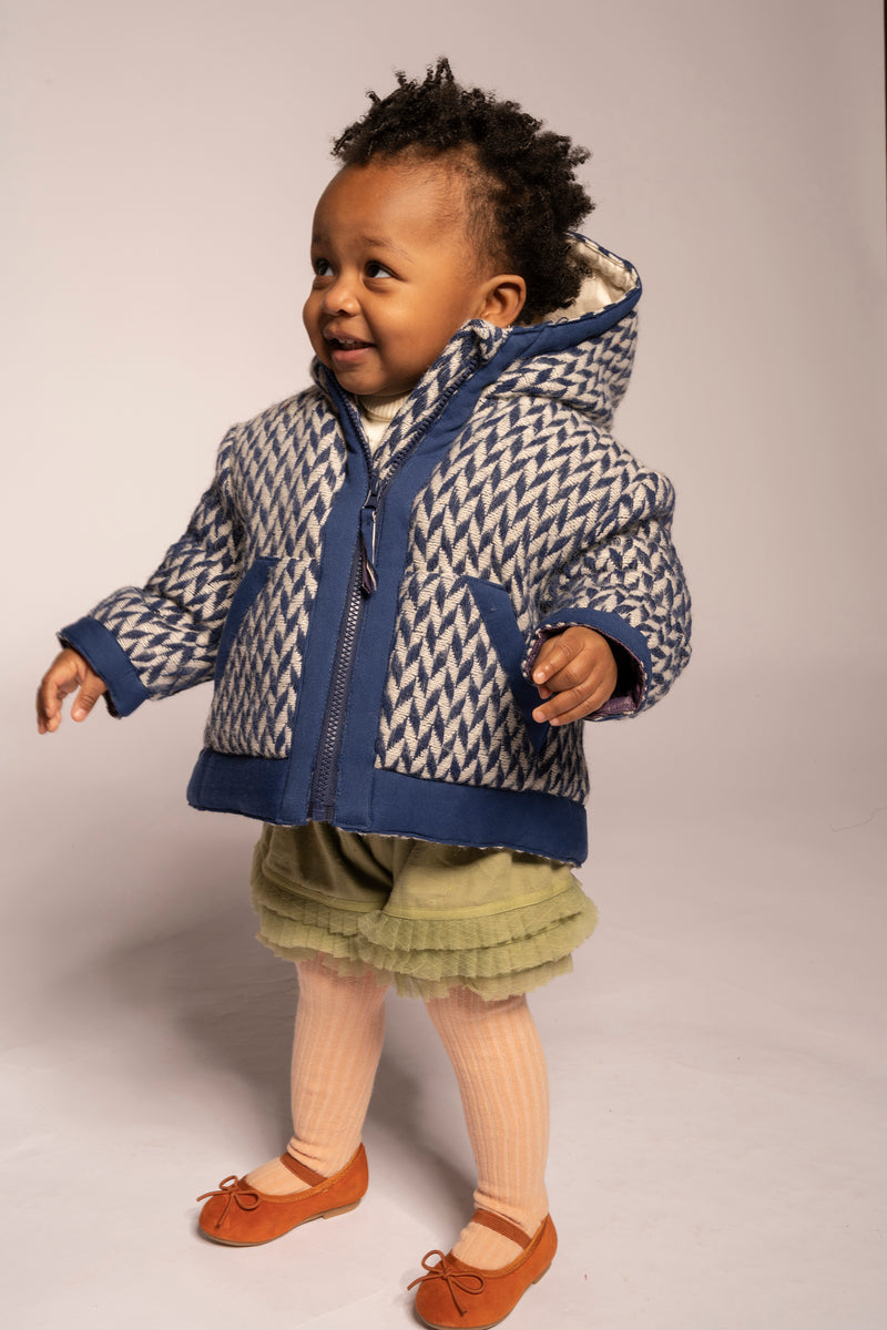 baby girl wearing padded winter coat in blue and white herringbone wool fabric with hood