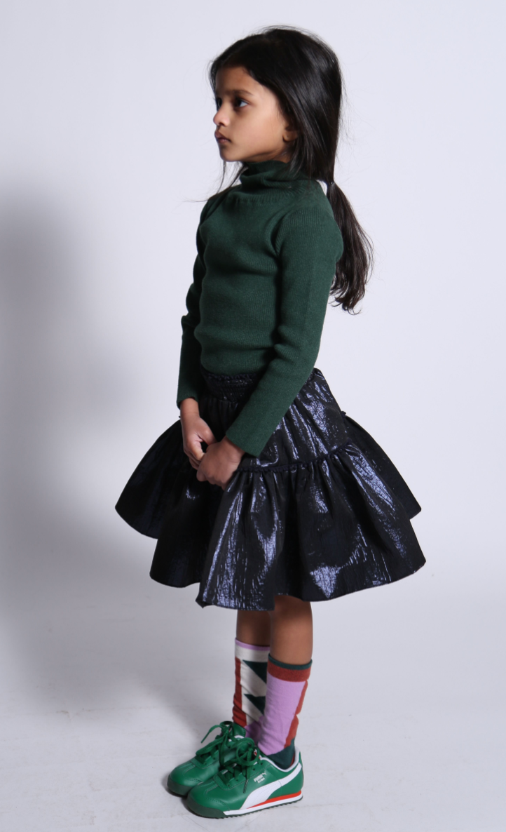 girl wearing green ribbed turtleneck and skirt with smocked waistband in navy blue shiny polyester fabric
