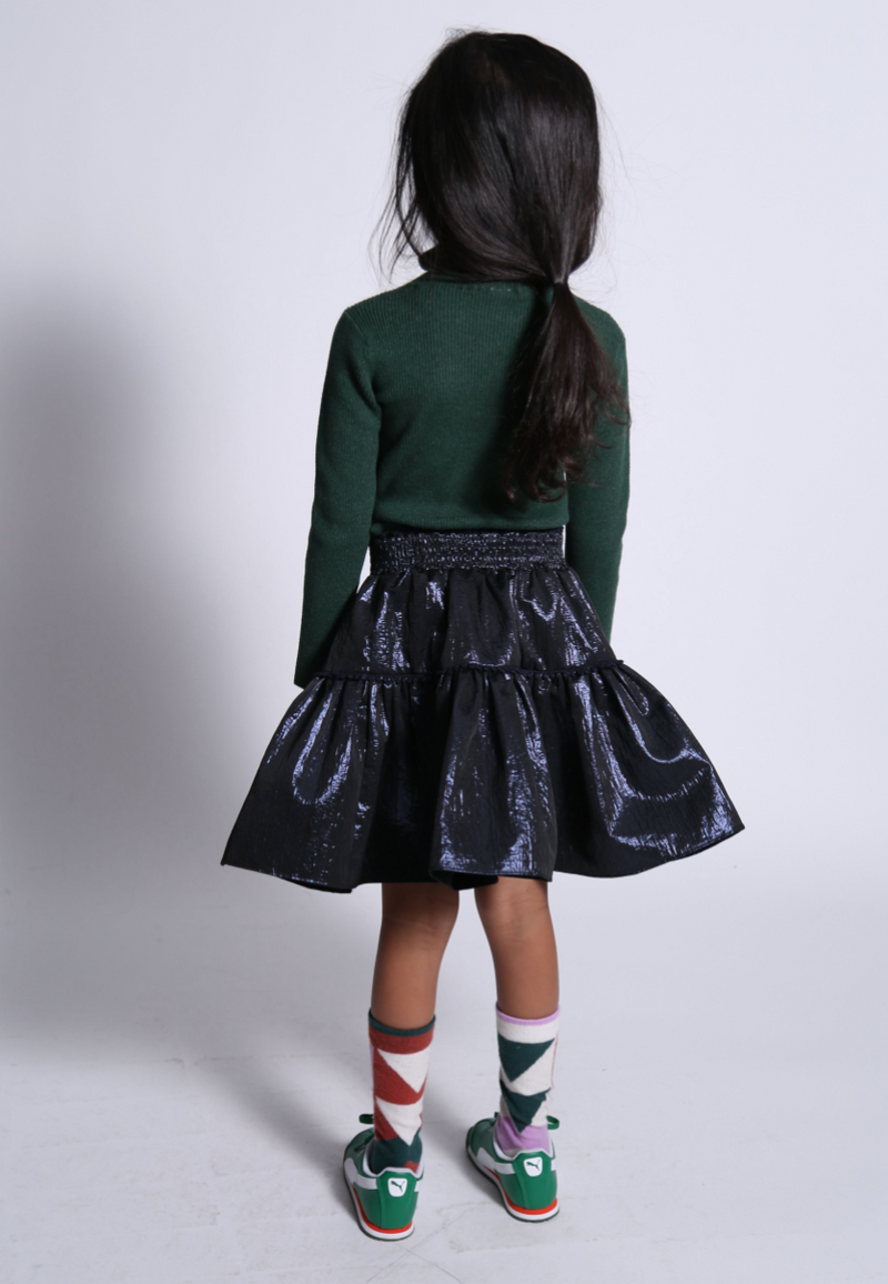 girl wearing green ribbed turtleneck and skirt with smocked waistband in navy blue shiny polyester fabric