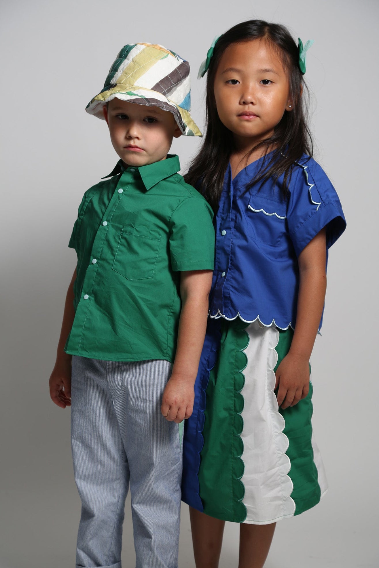 Two children wearing colorful outfits against a plain background