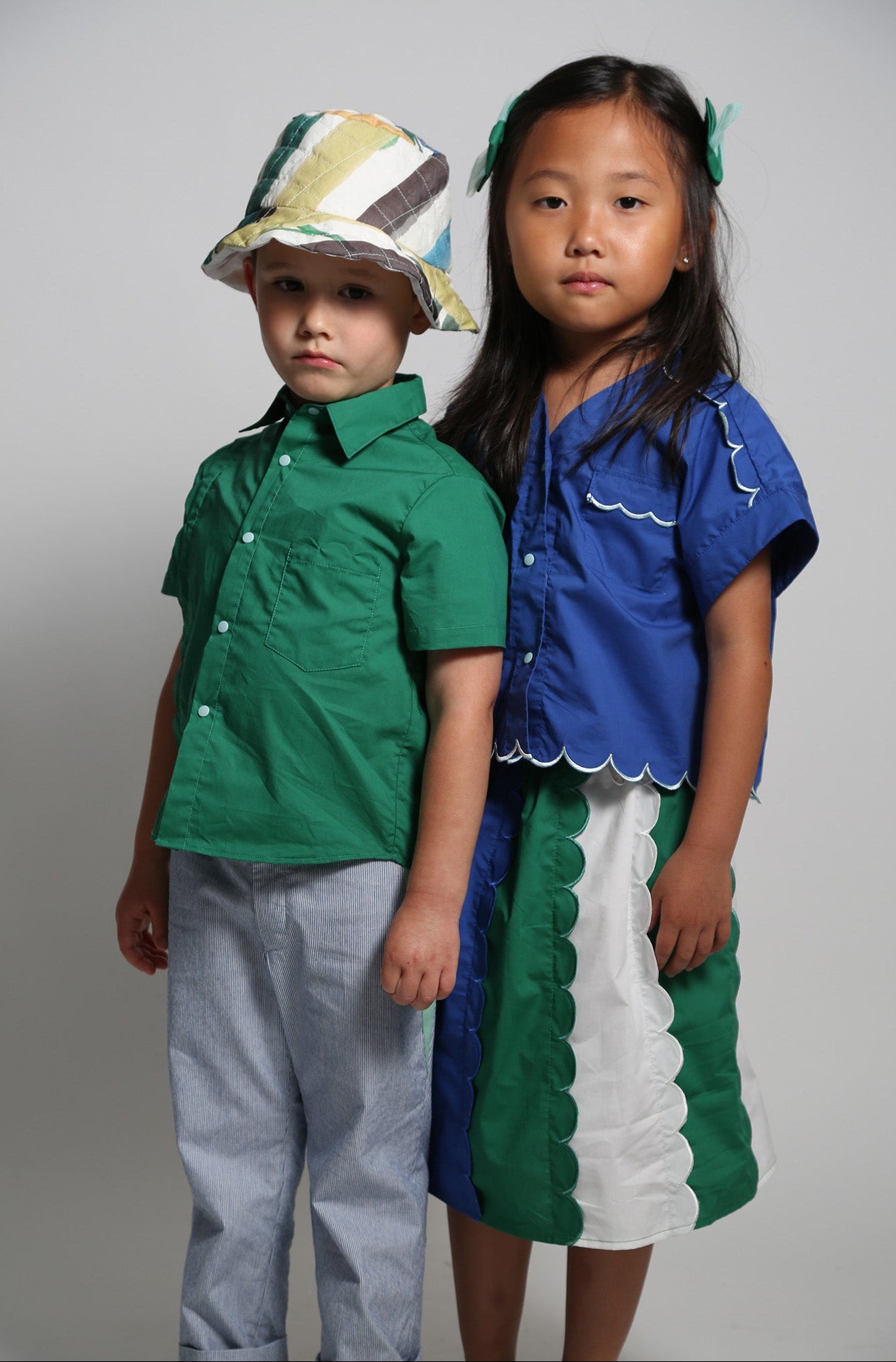 Two children wearing colorful outfits against a plain background