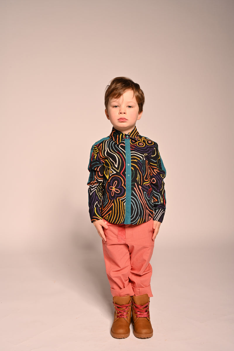 Boy wearing collared snap button down shirt with all over print in fine corduroy with red pants