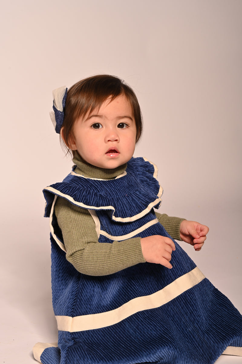 baby girl wearing corduroy blue dress with white ribbon stripes going across