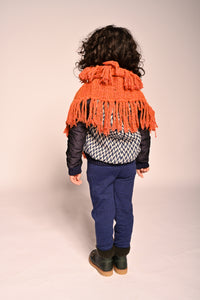 boy wearing orange hand knit wool slip over shrug with tassels